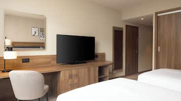 Ein Hotelzimmer mit einem Bett, einem Schreibtisch, einem Fernseher, einem Sessel und einem Kleiderschrank.