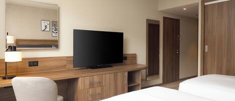 Una habitación de hotel con cama, escritorio, televisor, silla y armario.