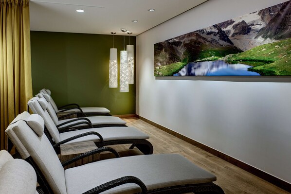 A room with a row of chairs, a painting of a mountain landscape, and pendant lights.