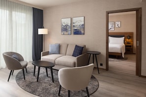 Habitación de hotel con sofá, dos sillones, una mesita, una lámpara y una cama con cabecero de madera.
