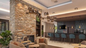 A modern interior with a stone wall, a fireplace, comfortable seating, and a bar area. - Hilton Garden Inn Davos (Davos)