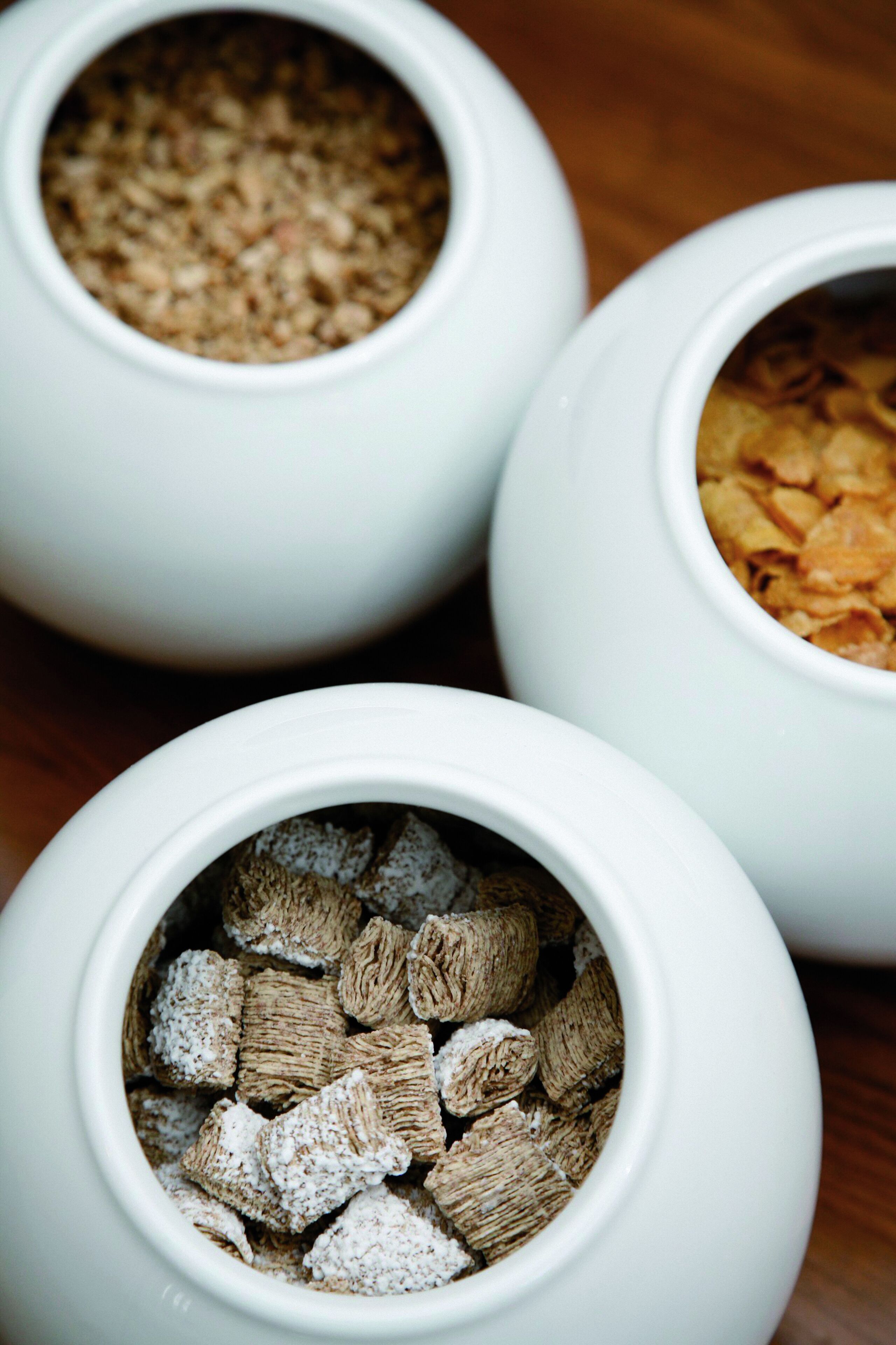 Three white ceramic bowls containing different types of cereal.