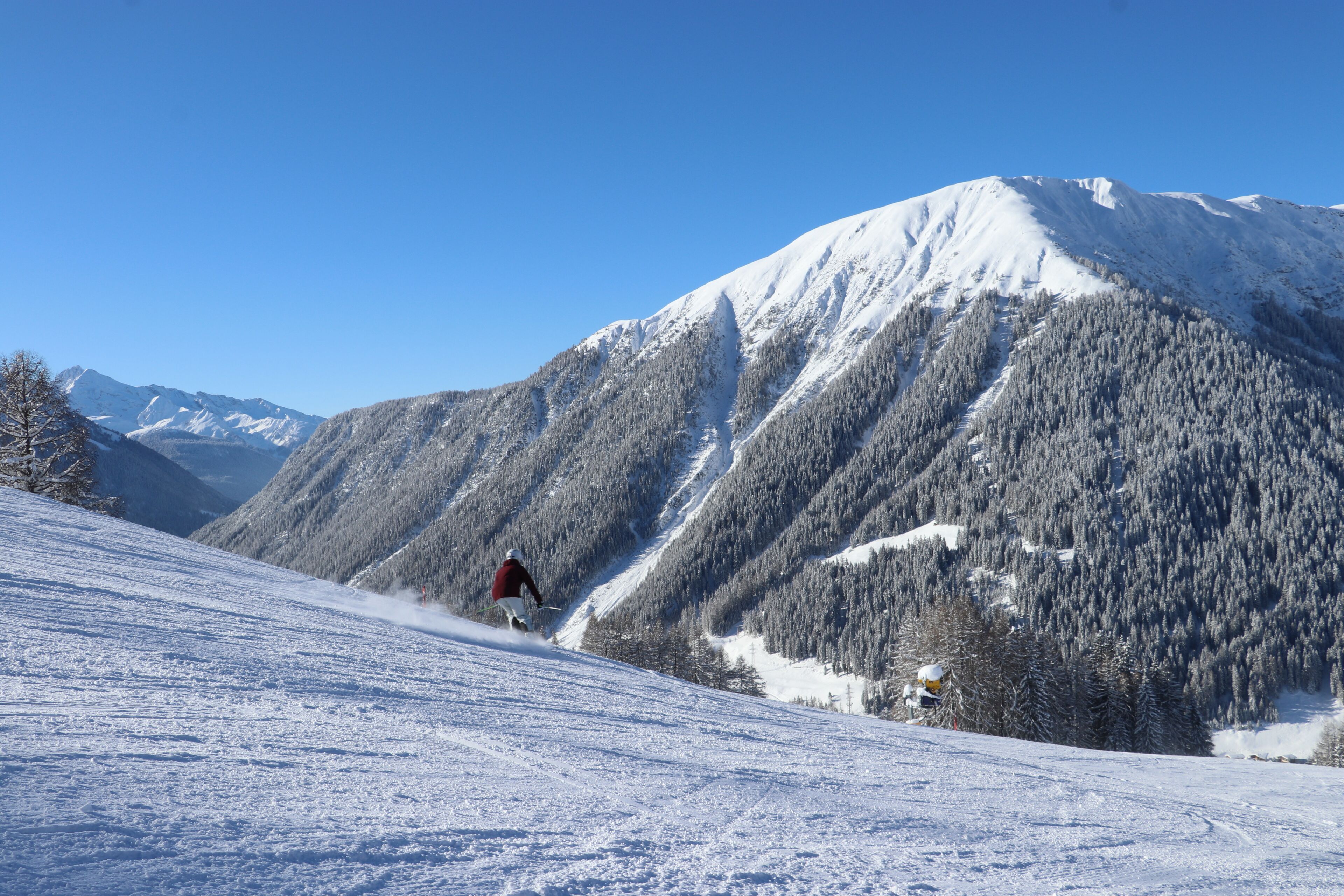 A snow-covered mountain slope with a skier in motion.