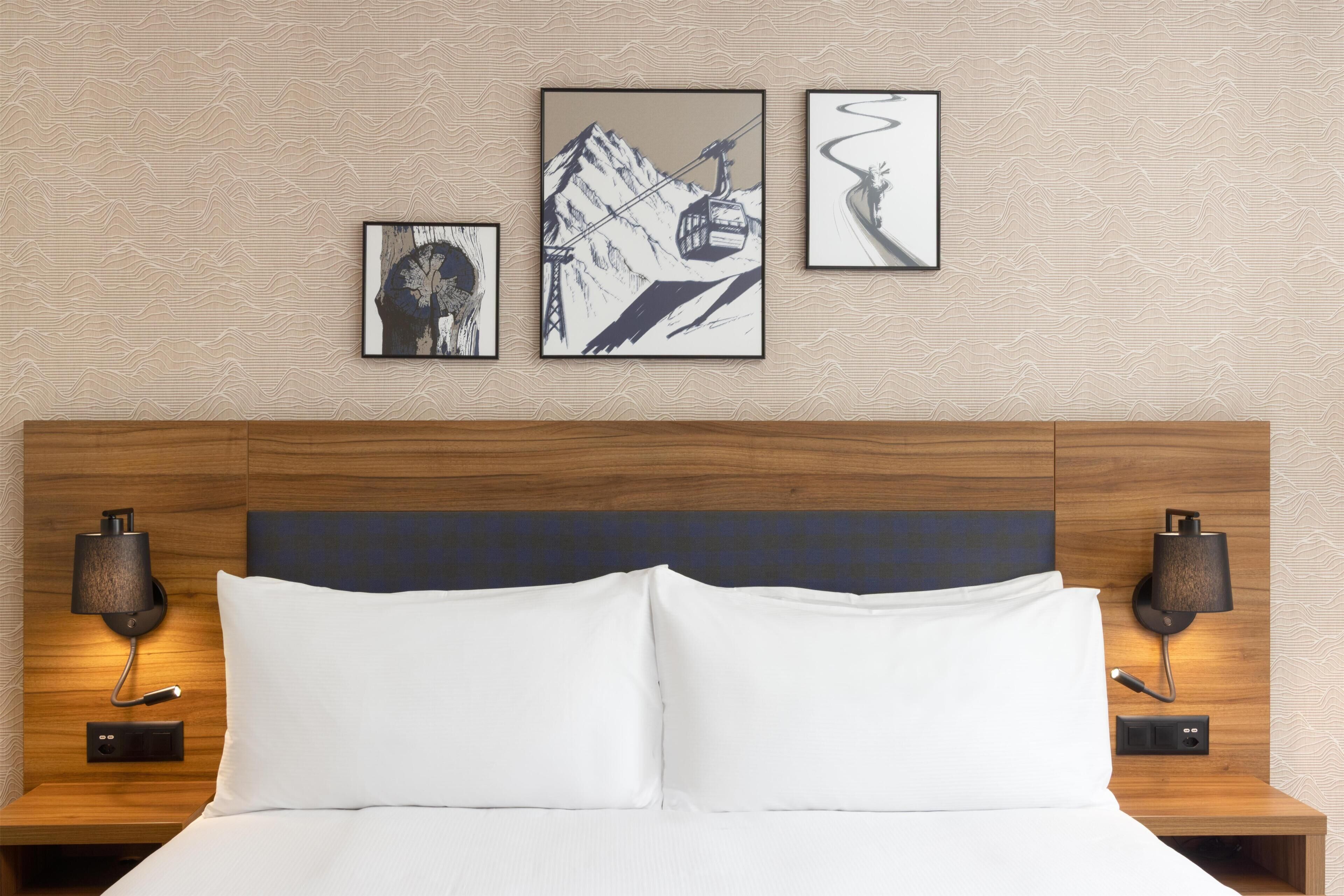 Una habitación de hotel con una cama, dos lámparas de pared y tres cuadros colgados.