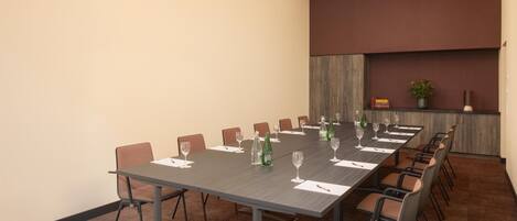 A conference room with a long table, chairs, and a plant on a shelf.