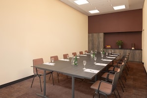 A conference room with a long table, chairs, and a plant on a shelf.