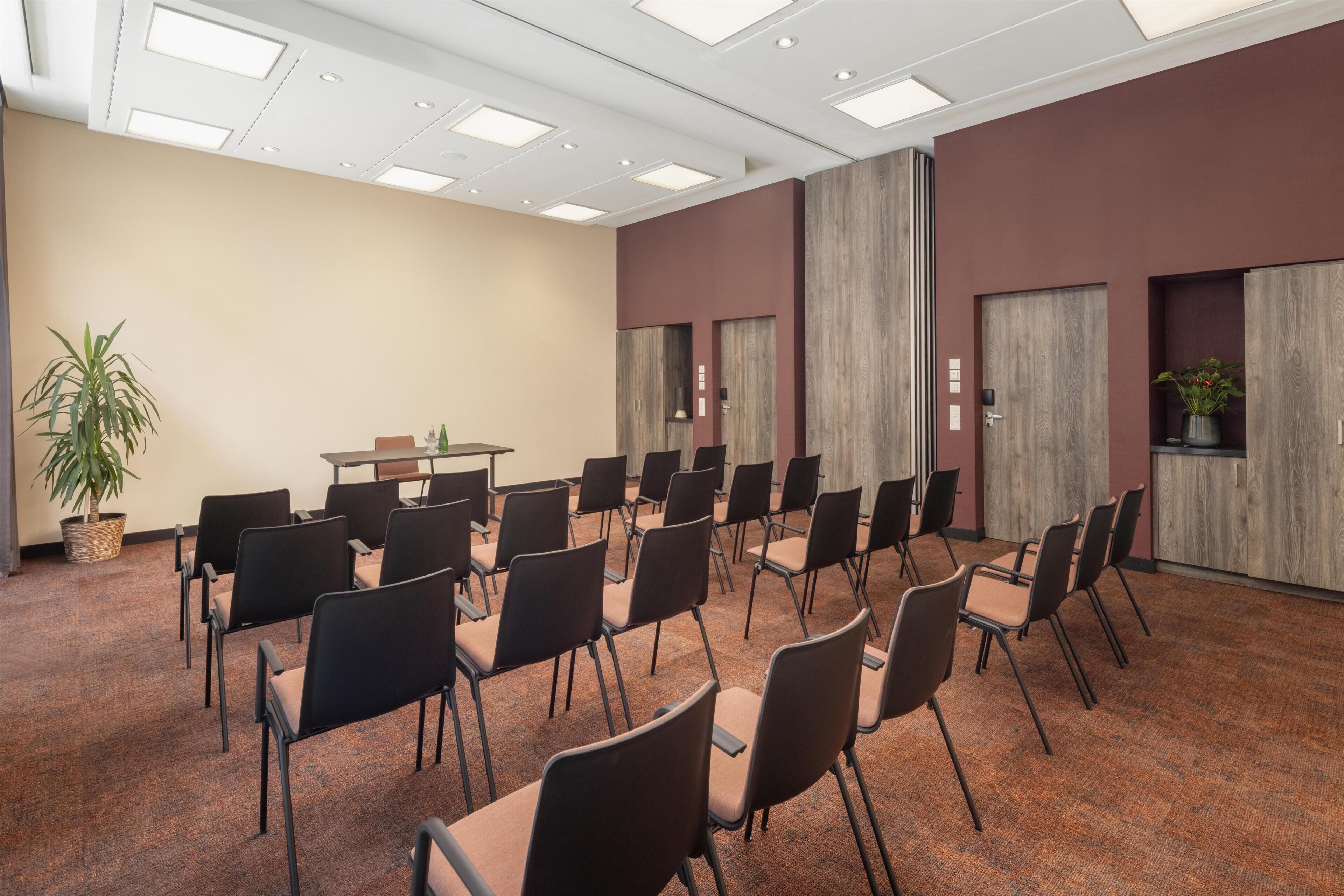 Un salón de conferencias con filas de sillas, una mesa y una planta en maceta.