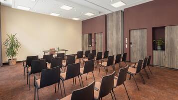Un salón de conferencias con filas de sillas, una mesa y una planta en maceta.