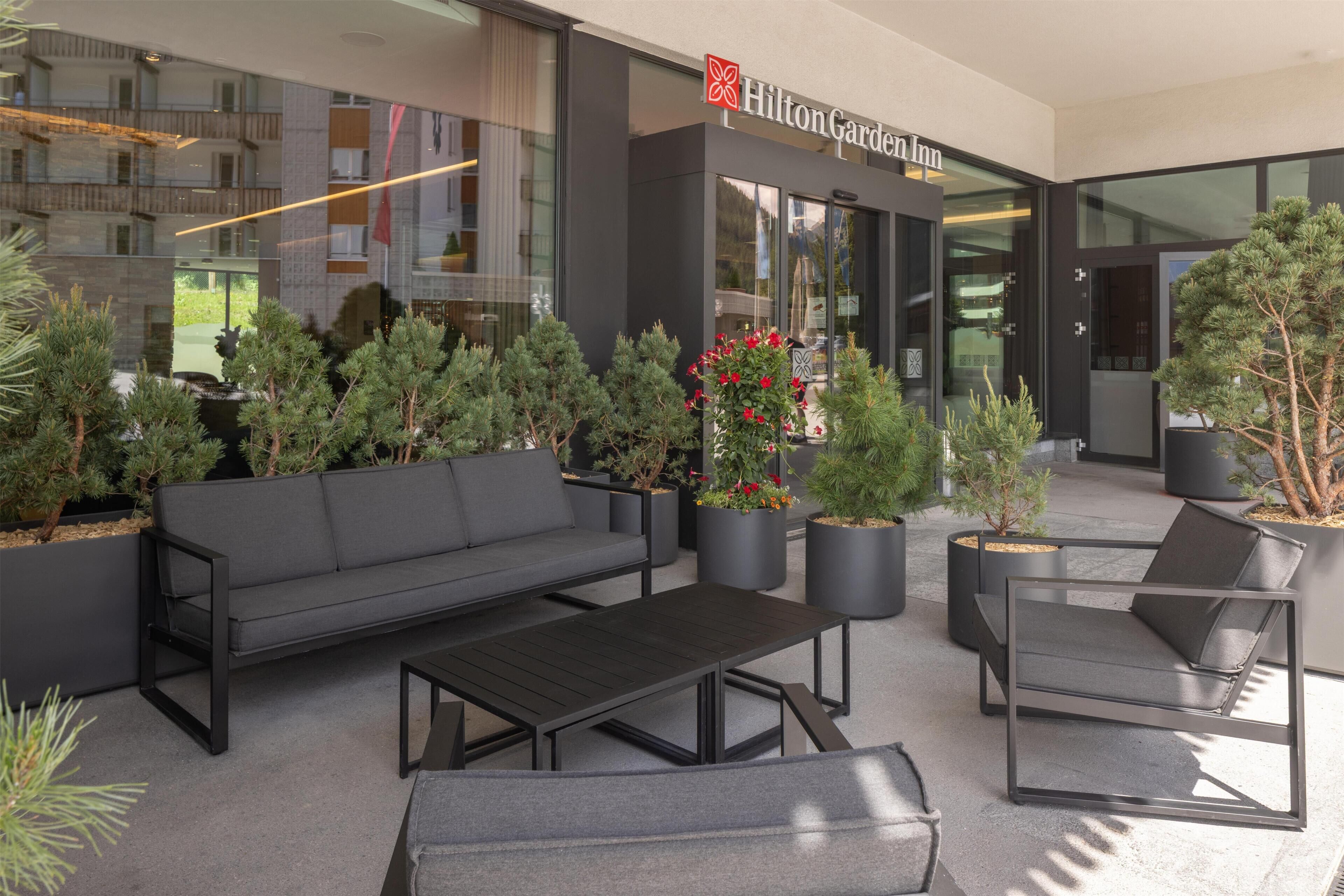 Un área de estar al aire libre con sofá, sillas y una mesa frente a un Hilton Garden Inn.