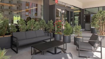 Un área de estar al aire libre con sofá, sillas y una mesa frente a un Hilton Garden Inn.