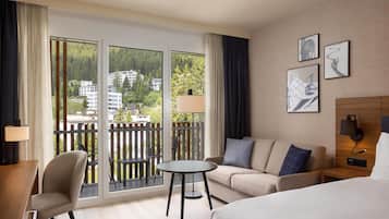 Ein Hotelzimmer mit Balkon, einer Couch, einem kleinen Tisch, einem Bett und einem Nachttisch.