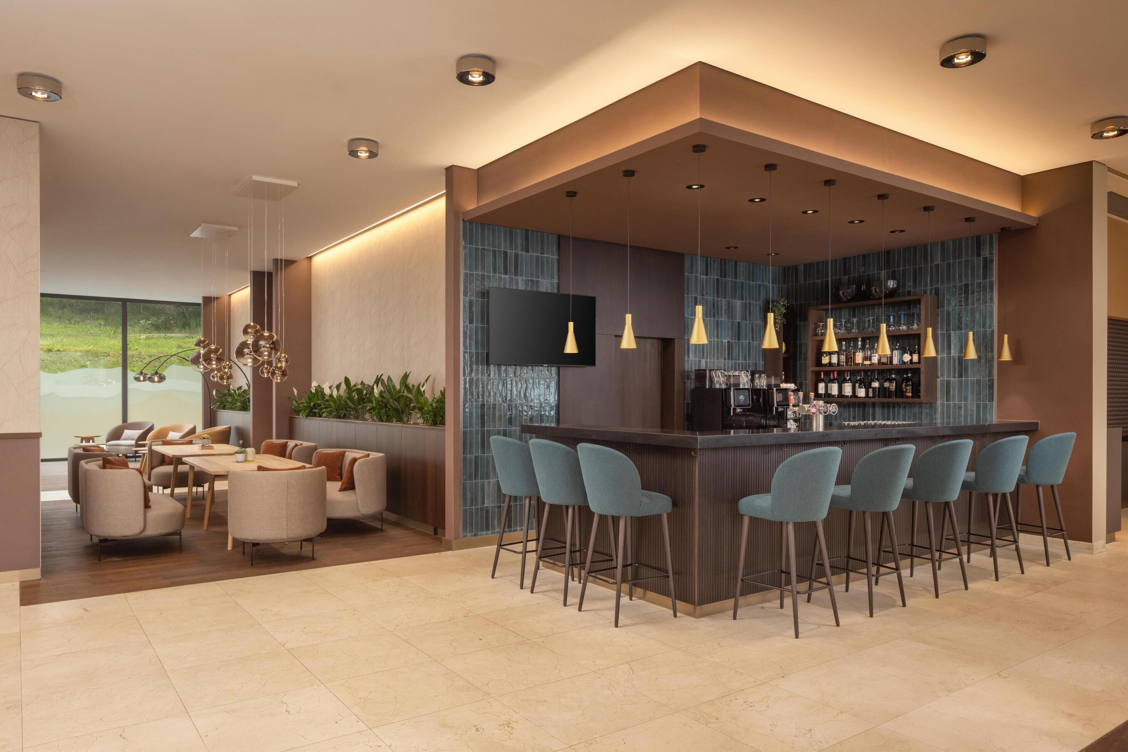 Zona de bar moderna con mostrador, varios taburetes e iluminación colgante.