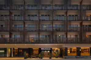 A multi-story hotel with a modern design, featuring balconies with vertical wooden slats, a well-lit entrance, and a visible signage for the Hilton Garden Inn. - Hilton Garden Inn Davos (Davos)