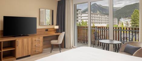 Habitación de hotel con una cama grande, televisión, escritorio con silla y balcón con mesa y sillas.