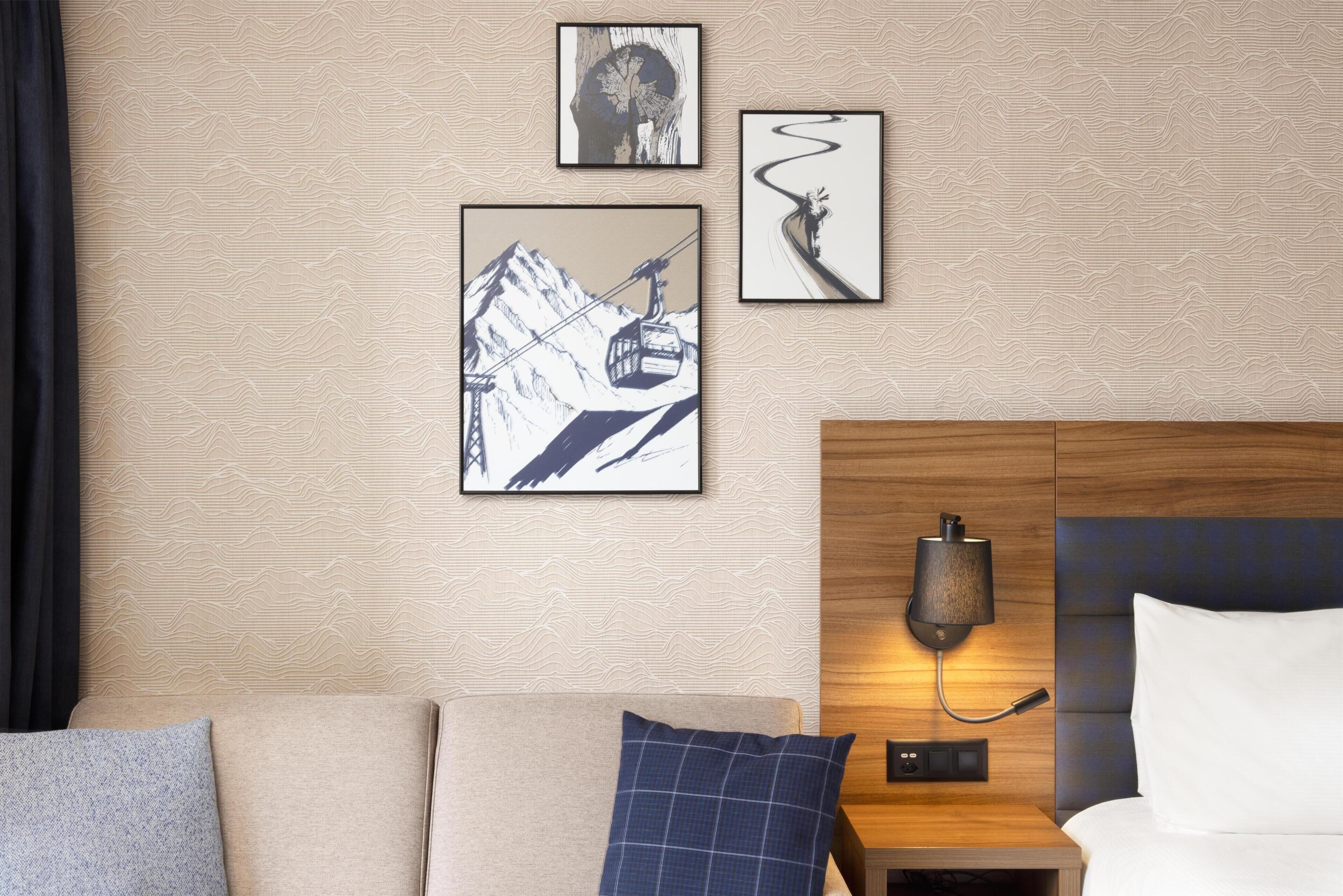A hotel room with a bed, a nightstand with a lamp, and three framed artworks on the wall.