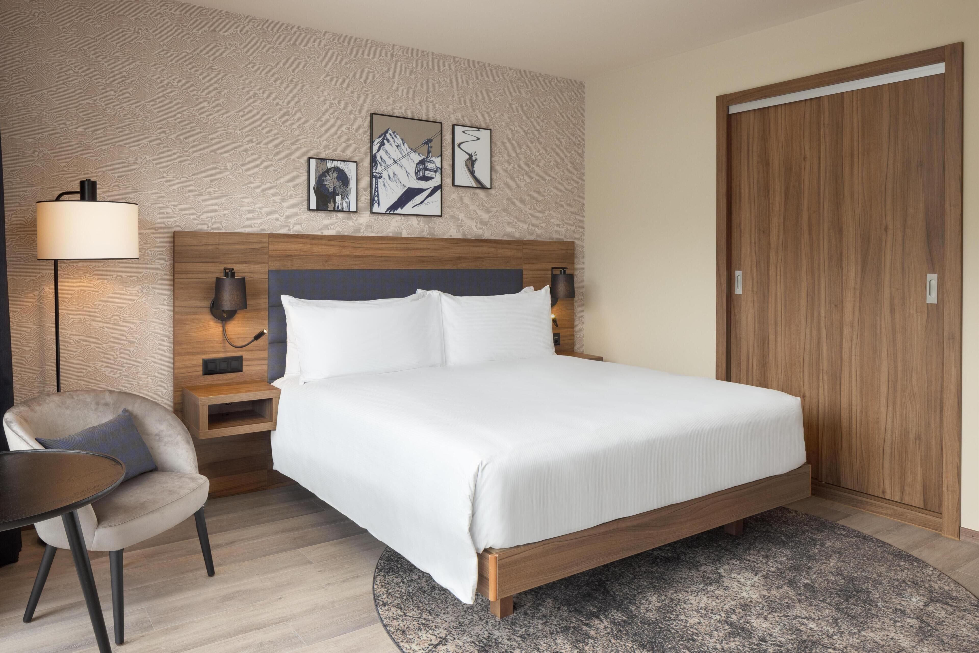 Una habitación de hotel con cama, mesitas de noche, una silla y una obra de arte en la pared.