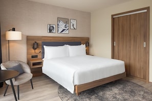 Una habitación de hotel con cama, mesitas de noche, una silla y una obra de arte en la pared.