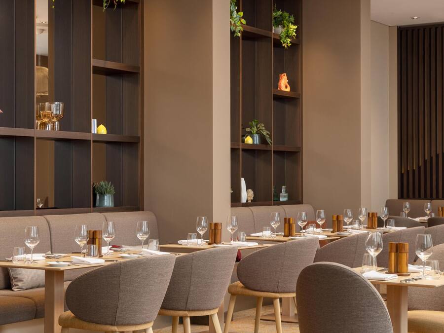 Ein modernes Restaurantinterieur mit einem langen Esstisch, mehreren Stühlen und verschiedenen Dekorationen auf Regalen.