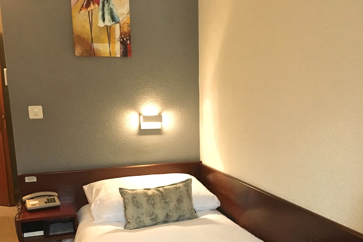 Een hotelkamer met een bed, nachtkastje, lamp en kunst aan de muur.