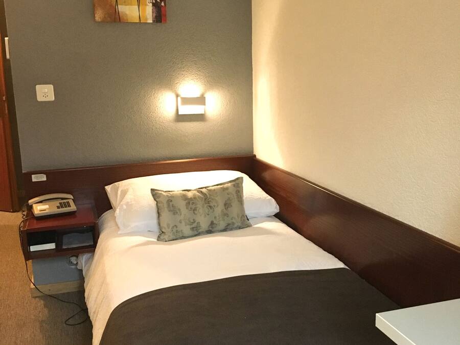 Una habitación de hotel con cama, mesita de noche, lámpara y una obra de arte en la pared.