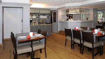 Une cuisine moderne dotée d’un îlot central, d’un coin repas avec des tables et des chaises en bois, et d’un bar avec un comptoir et des étagères.