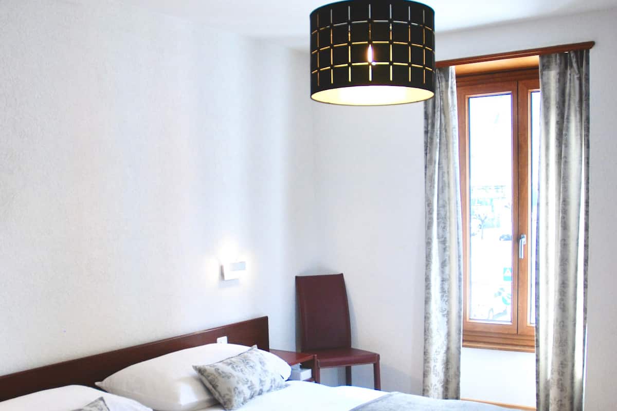 Een slaapkamer met een groot bed, een stoel, een hanglamp en een raam met gordijnen.