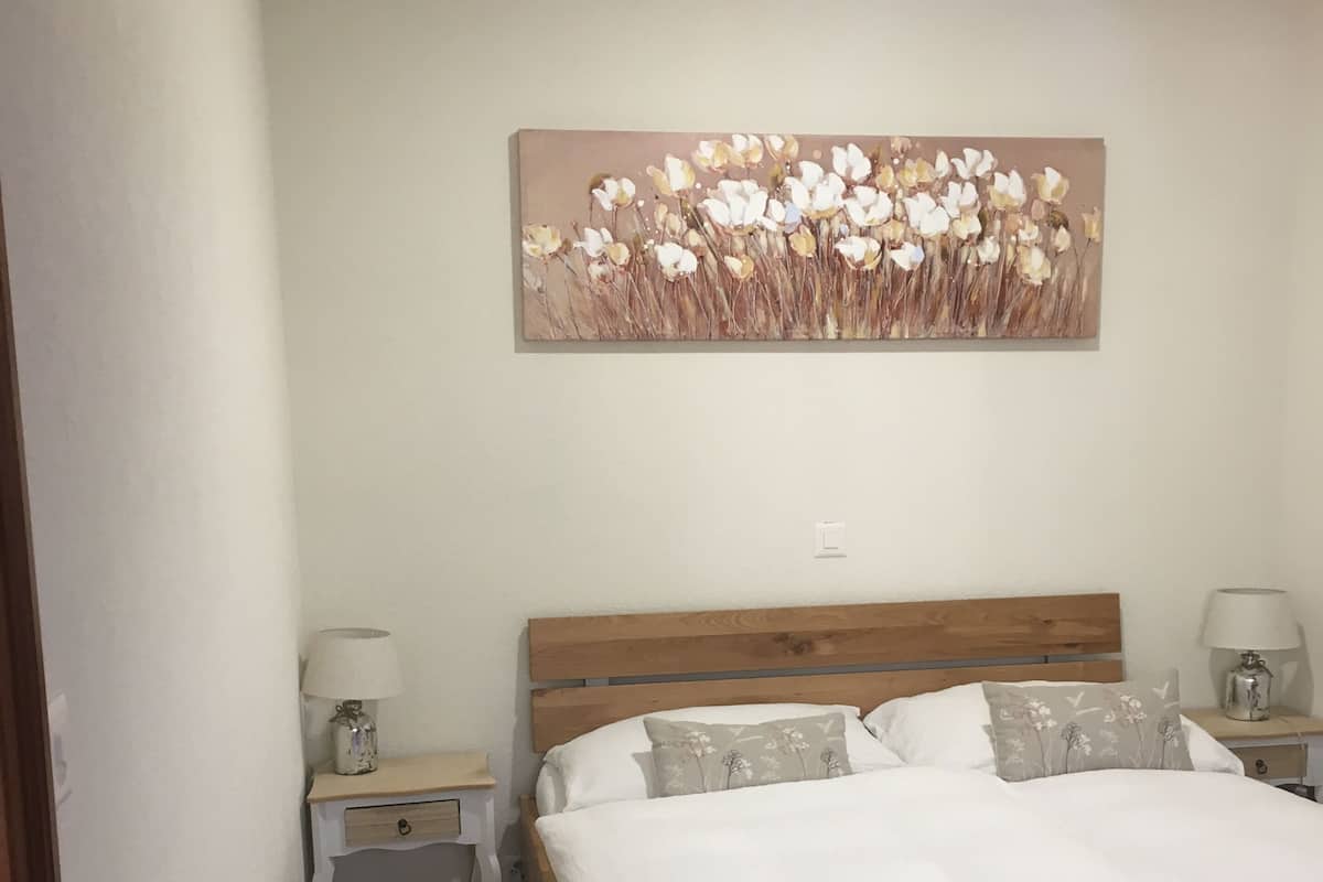 Een slaapkamer met een houten bed, witte beddengoed, twee nachtkastjes met lampen, en een bloemendecoratie aan de muur.