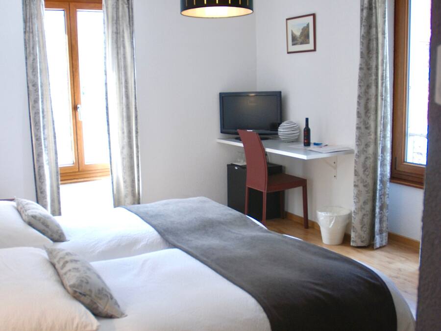 A bedroom with a bed, a desk, a chair, a television, and a window with curtains.