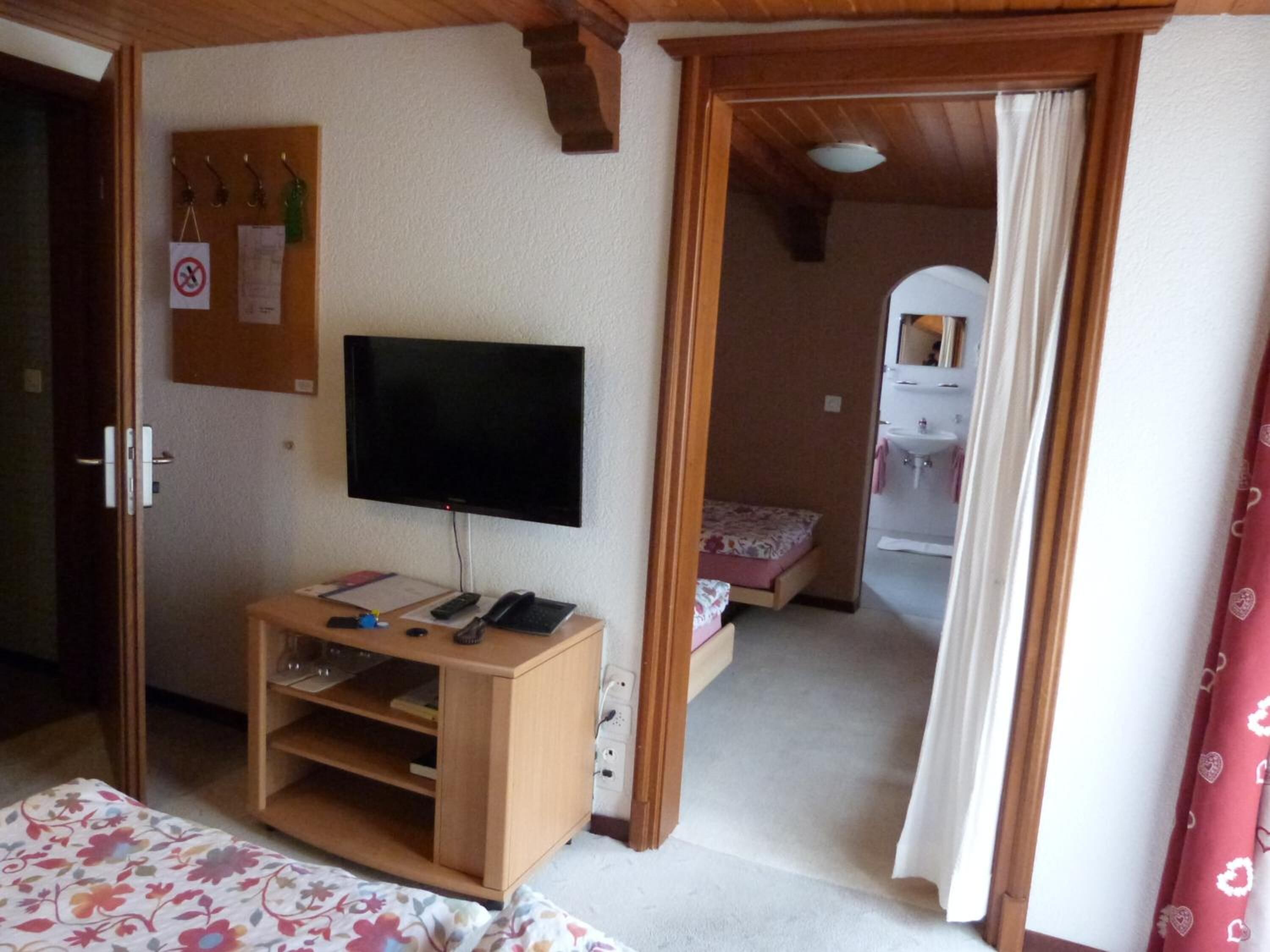 Una habitación con una cama, un televisor sobre un mueble de madera, un escritorio con un teléfono y una mesita de noche.