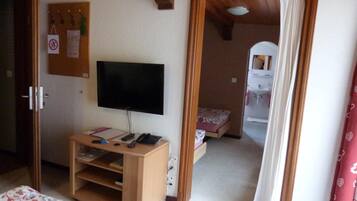 Une chambre avec un lit, un téléviseur posé sur un meuble en bois, un bureau avec un téléphone et une petite table de chevet.