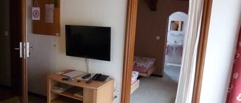 Una habitación con una cama, un televisor sobre un mueble de madera, un escritorio con un teléfono y una mesita de noche.