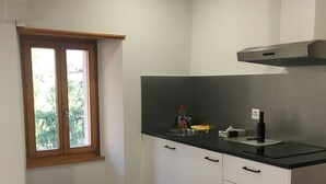 A bedroom with two beds, a kitchenette with a stove, and a window with a view of greenery.