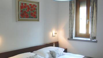A bedroom with a bed, a hanging light fixture, a window with curtains, and a framed painting on the wall.