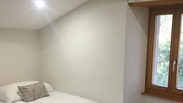 A bedroom with a single bed, a window with a view of greenery, and a sloped ceiling.