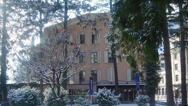 A hotel with a traditional facade, multiple windows, and a snow-covered garden.