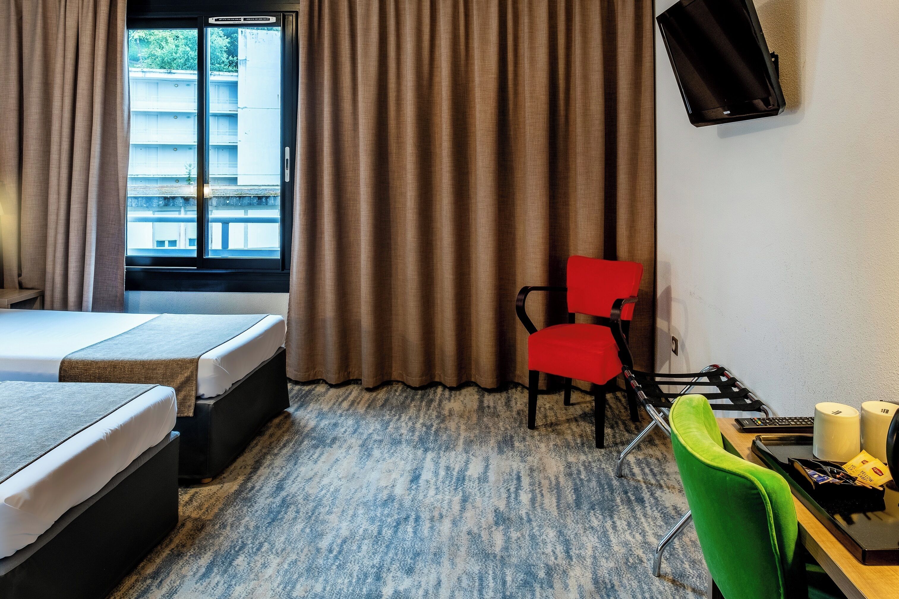 Habitación de hotel con dos camas, un escritorio con silla, televisor y ventana con cortinas.