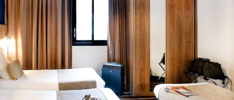 Habitación de hotel con dos camas, un armario, una maleta y una silla.