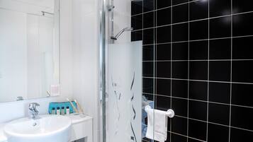 A bathroom with a white sink, a glass shower enclosure, and black tiled walls.