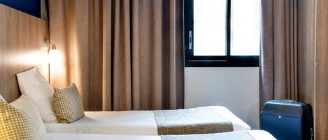 Une chambre d’hôtel avec deux lits, une fenêtre avec des rideaux, une lampe et une valise.
