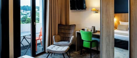 A hotel room with a bed, a desk, a television, and a view of the city through the window.