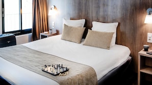 A neatly made bed with a chessboard, a wooden headboard, and a nightstand with a lamp. - Hotel Panorama (Lourdes)