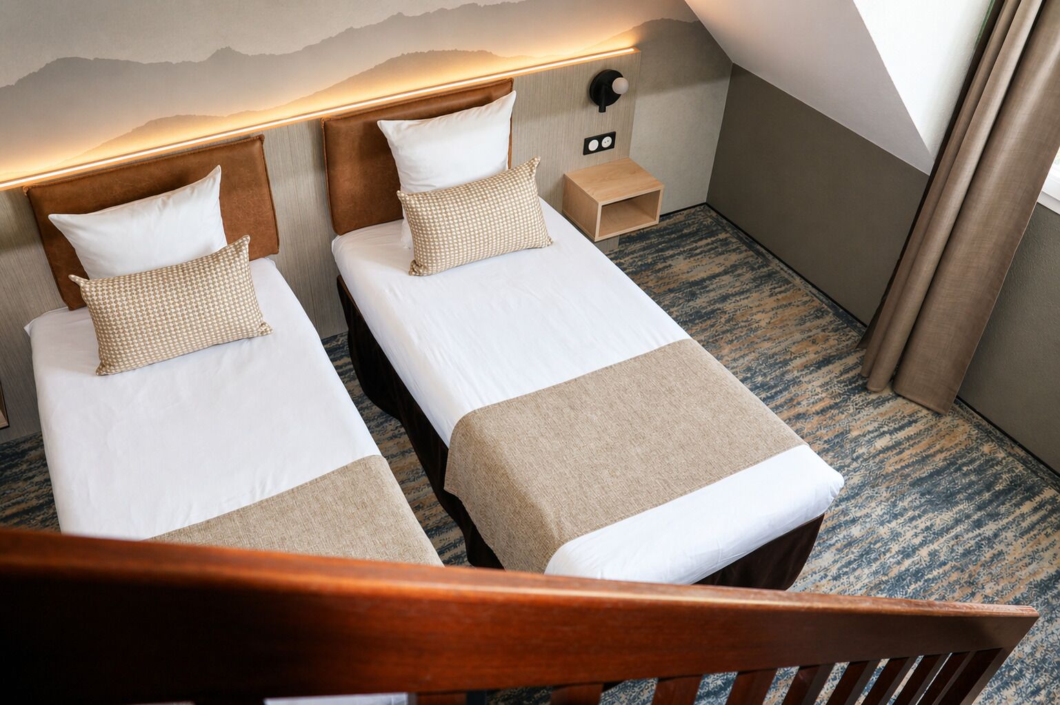 A hotel room with two beds, a nightstand, a wall-mounted light, and a view of the mountains.