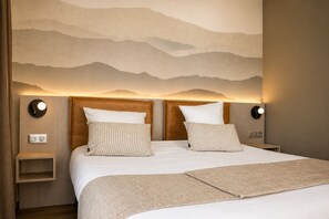 A hotel room with a bed, two pillows, a headboard, bedside tables, wall-mounted lights, and a mountain mural. - Hotel La Solitude (Lourdes)
