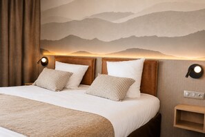 Une chambre d’hôtel comprenant un lit, deux oreillers, une table de chevet, une lampe fixée au mur et un mur décoratif.