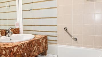 A bathroom with a marble sink, a handrail, and a bathtub.