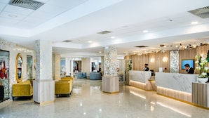 A hotel lobby with marble reception desks, gold-toned sofas, and a polished floor. - Hotel La Solitude (Lourdes)