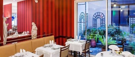 A restaurant with red striped walls, white tables, and a view of a garden through large windows.