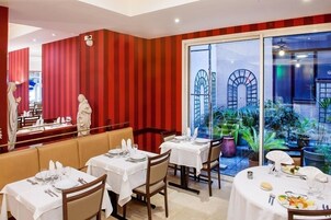 A restaurant with red striped walls, white tables, and a view of a garden through large windows.
