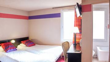 Une chambre d’hôtel avec deux lits, un bureau, une chaise et une salle de bain visible à travers une porte ouverte.