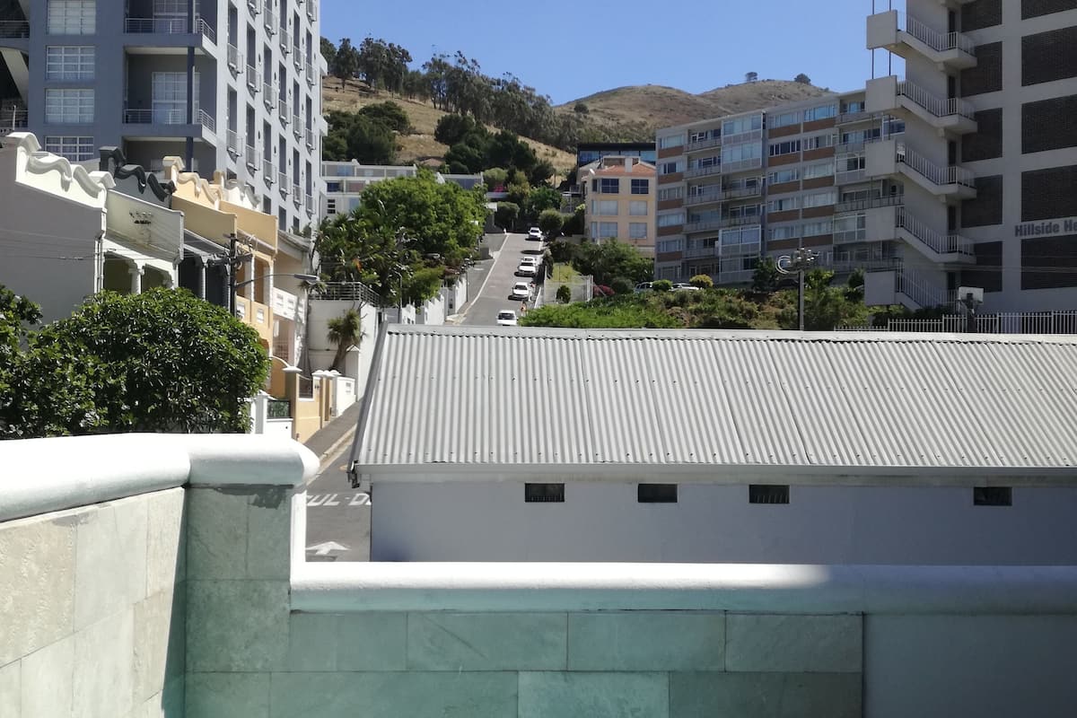 A swimming pool with a clear blue water, surrounded by buildings and a hilly landscape in the background.